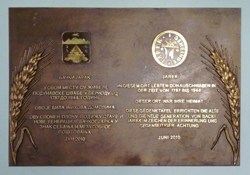 Picture 11 – The new Jarek Memorial plaque in the foyer of the town hall in Bački Jarak. Below both municipal coats-of-arms of Bački Jarak (left) and of Jarek (right) each contains the same text in the Serbian and German language.